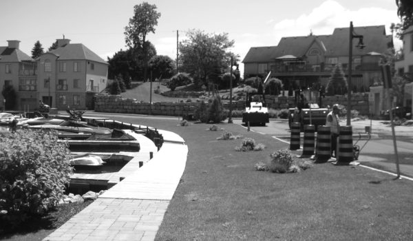 A black and white photo of a park with a boat in the water.